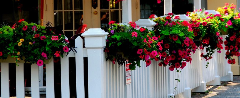 A picket fence surrounding a patio with several hanging flower baskets attached